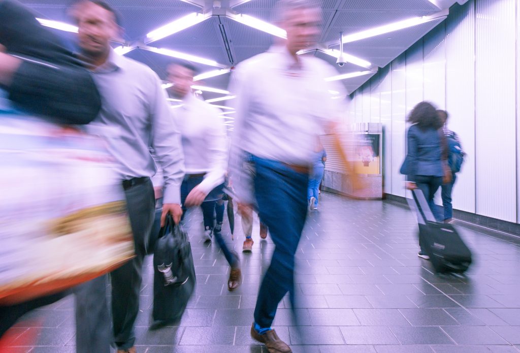 Blurry image of corporate professionals walking at a fast pace through a train station. The image is meant to portray the quick and immediate unconscious bias you will notice when first glancing at others.